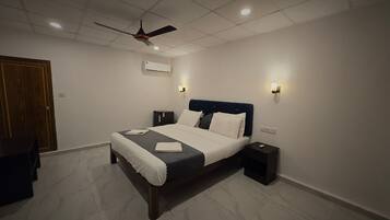 Un dormitorio con cama, mesitas de noche, ventilador de techo y aire acondicionado.