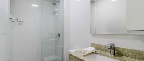 A modern bathroom with a glass-enclosed shower, a white sink with a granite countertop, and a large mirror above the sink.