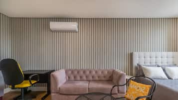 Una habitación con pared a rayas, un sofá con volantes, una cama con cabecera, un escritorio con silla y un equipo de aire acondicionado.