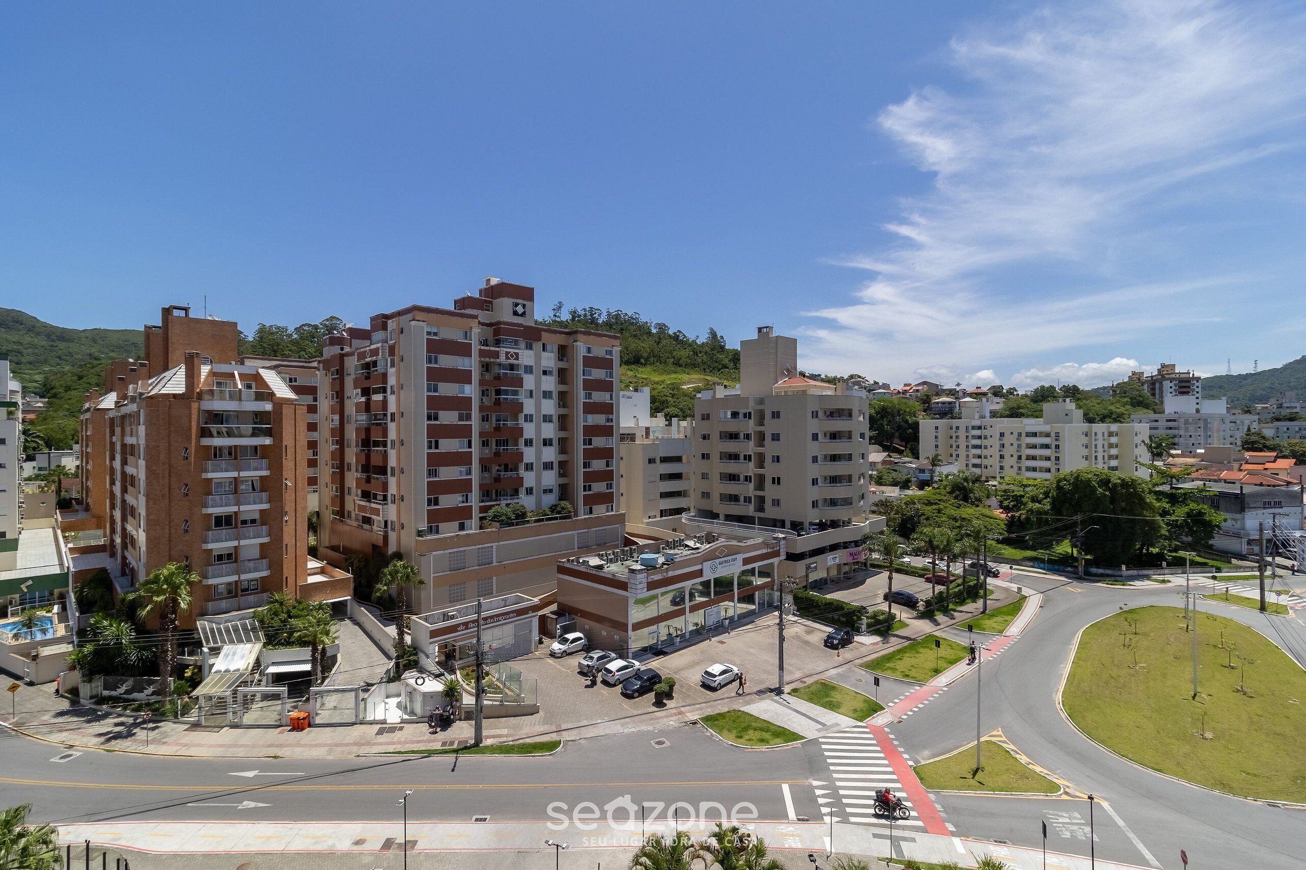 Un edificio de varios pisos con una planta baja comercial, rodeado por un parque arbolado y una glorieta.