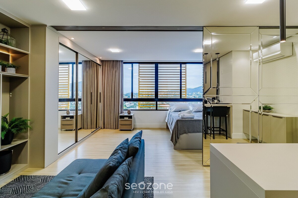 A modern hotel room with a large bed, a sofa, a desk, and a view of the city.