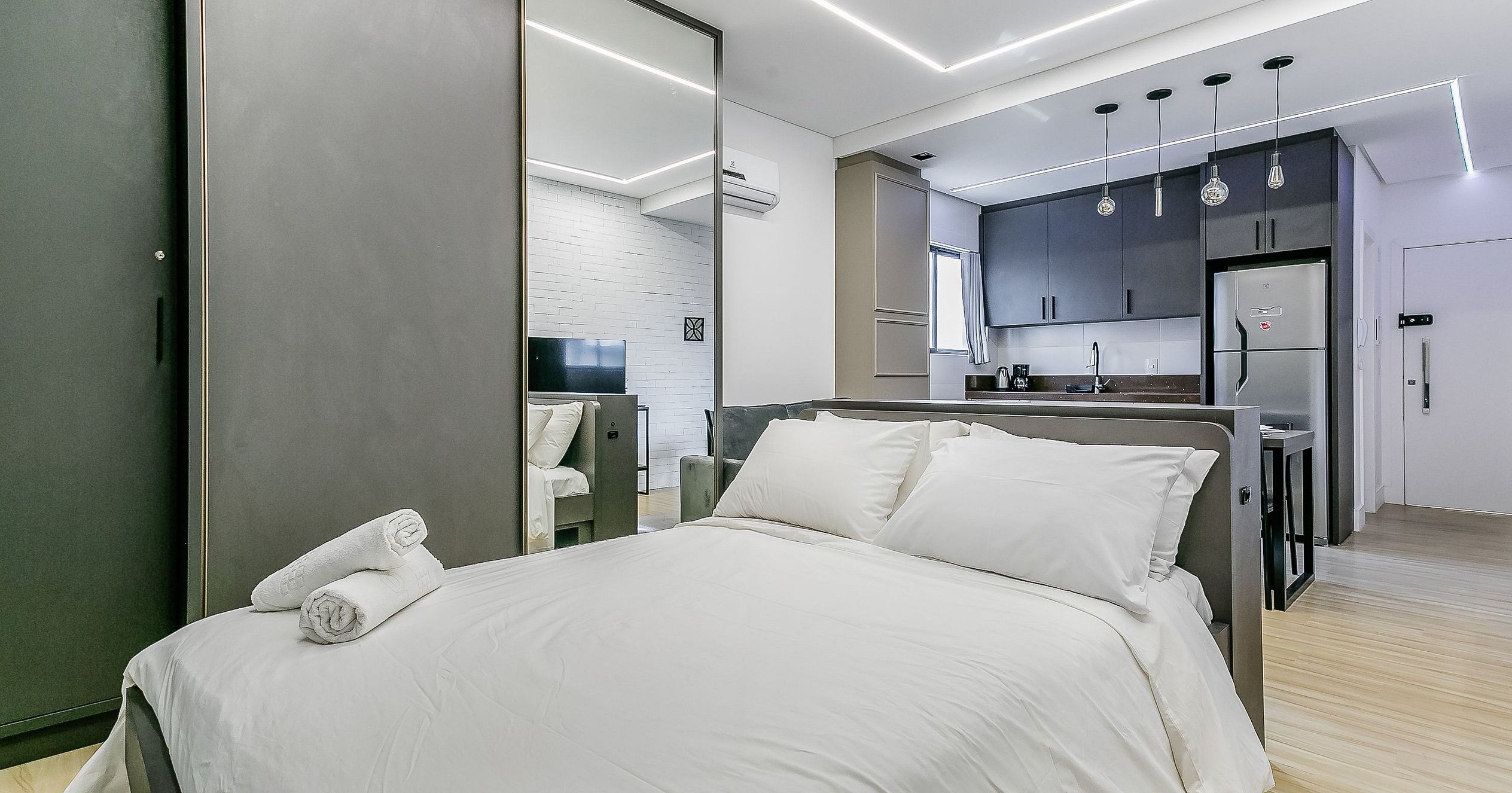 Un dormitorio moderno con cama, televisión de pantalla plana y una kitchenette al fondo.