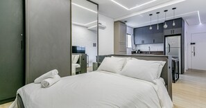 A modern bedroom with a bed, a TV, and a kitchenette.