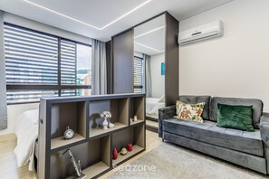 Una sala de estar moderna con un sofá gris, un armario espejado y un amplio ventanal con persianas.