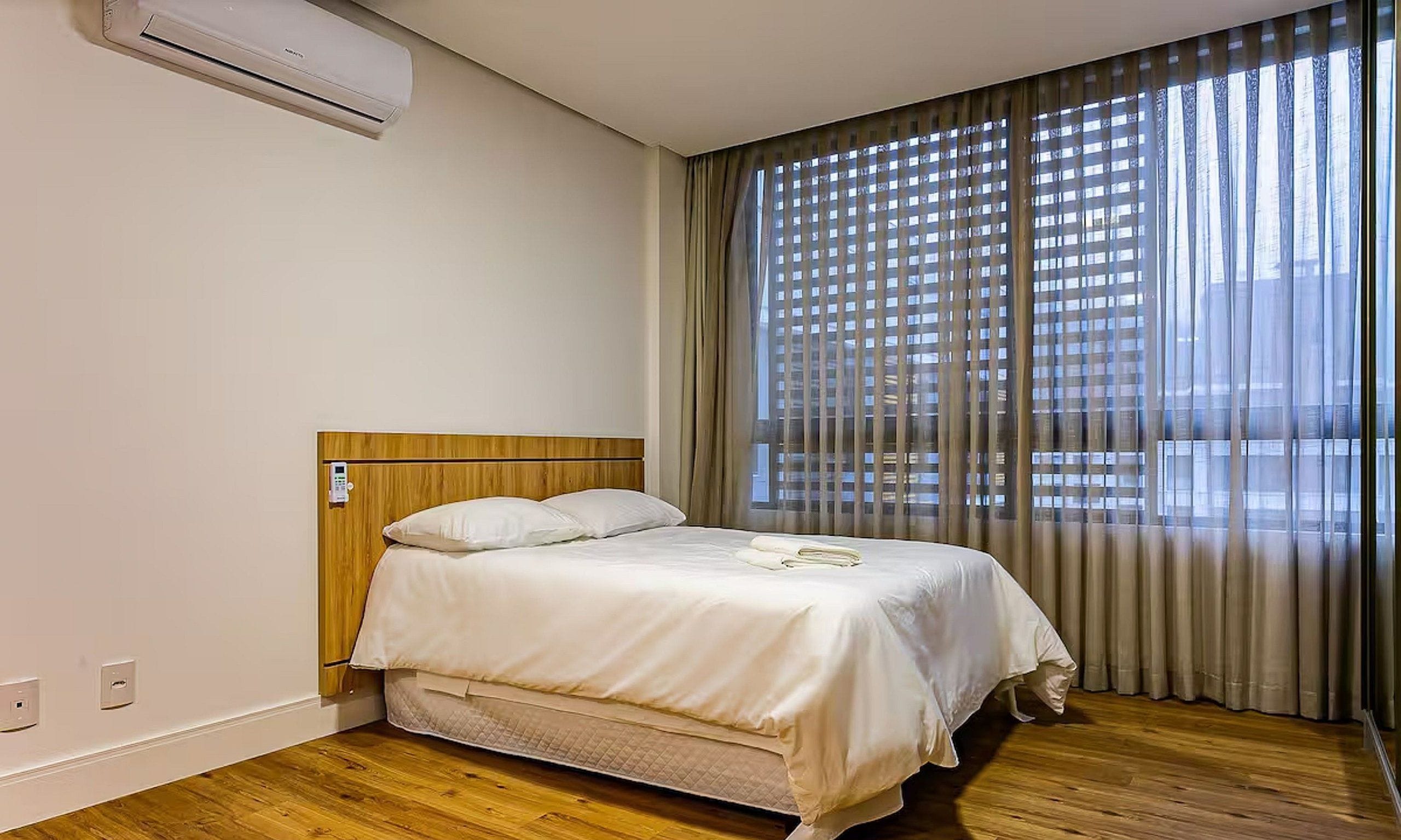 Una camera d'albergo con un letto, un pannello di controllo e una finestra con tende.