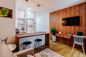 Una cocina moderna con un muro decorado con madera, un televisor de pantalla plana y un comedor con taburetes de bar.