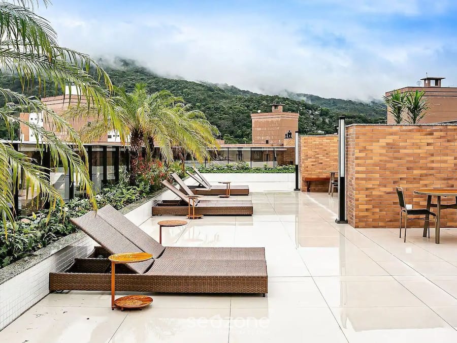 A rooftop terrace with lounge chairs, a dining table, and a view of a mountainous landscape.