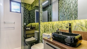 Une salle de bain avec des toilettes, un lavabo et un miroir. Les murs sont décorés d’un motif représentant des feuilles.