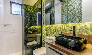 A bathroom with a toilet, sink, and mirror. The walls have a leafy pattern.