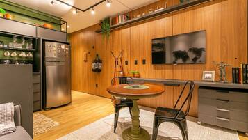 A modern kitchen with a built-in refrigerator, wooden cabinets, a dining table with chairs, and a TV mounted on the wall.