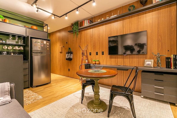 A modern kitchen with a built-in refrigerator, wooden cabinets, a dining table with chairs, and a TV mounted on the wall.