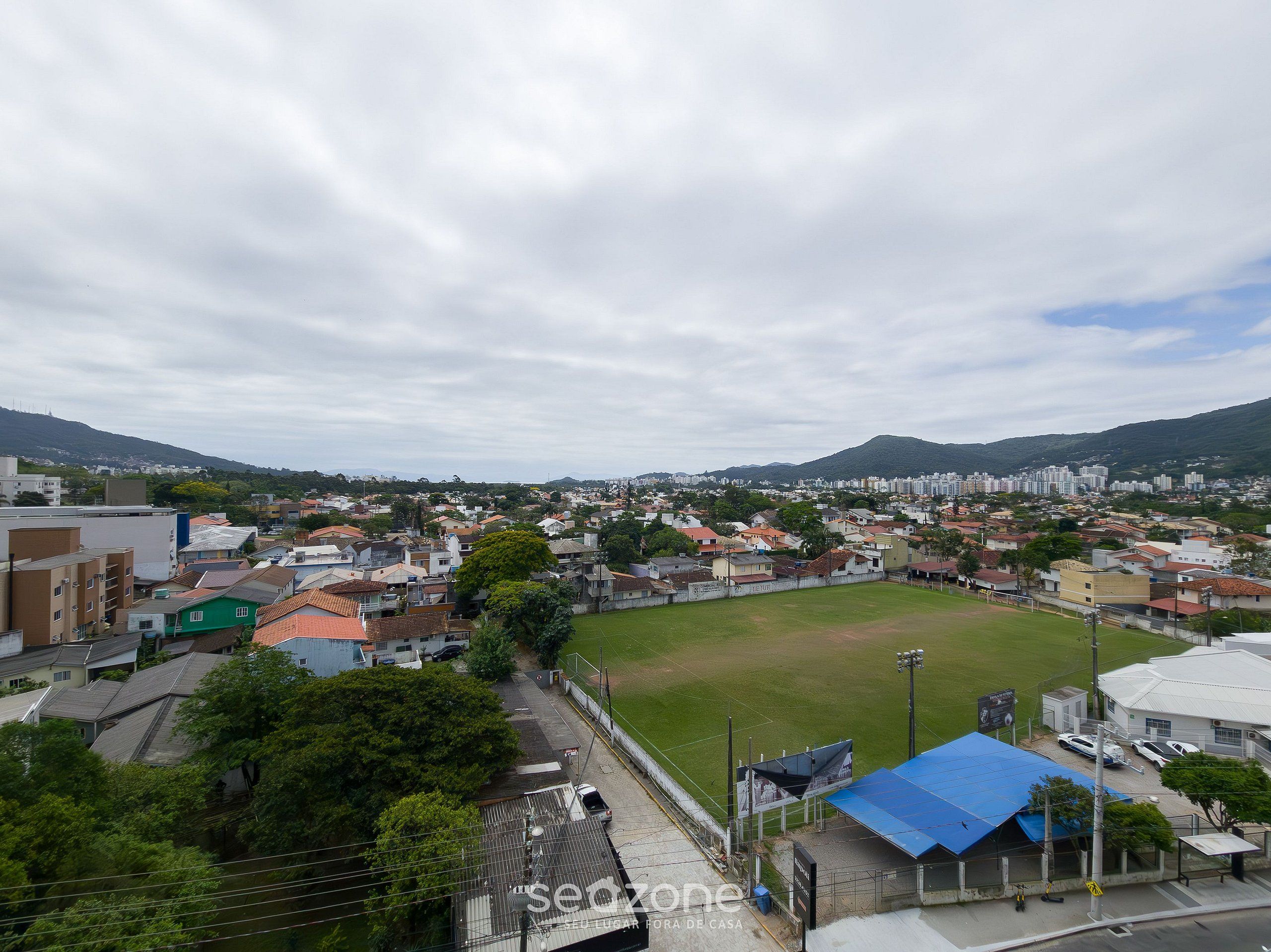 Un barrio residencial con casas, un campo deportivo y un paisaje montañoso al fondo.