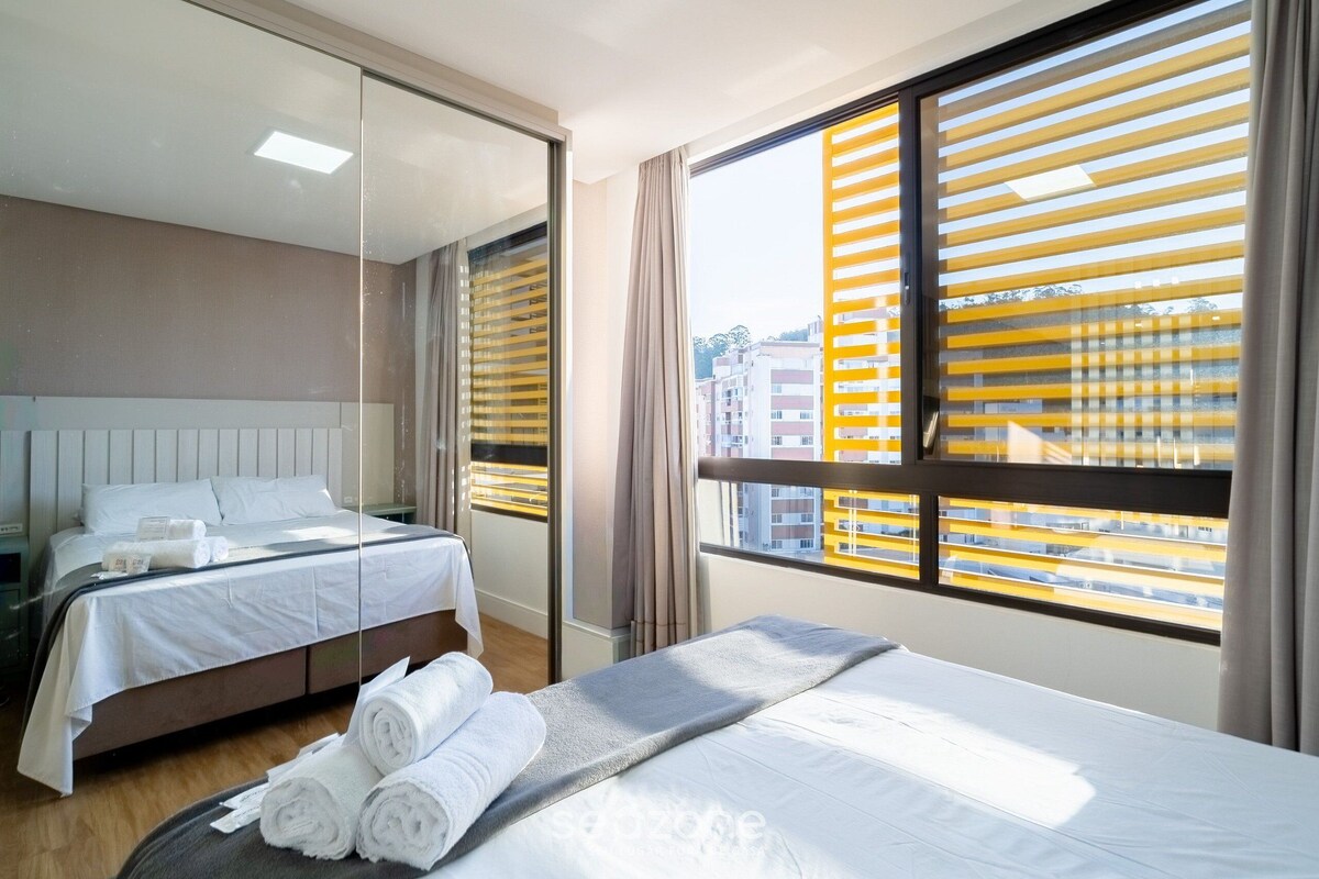 A hotel room with a large bed, a smaller bed, a mirror, and a window with blinds.