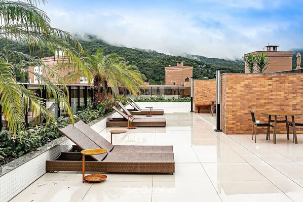 A rooftop terrace with lounge chairs, a dining table, and a view of a mountainous landscape.