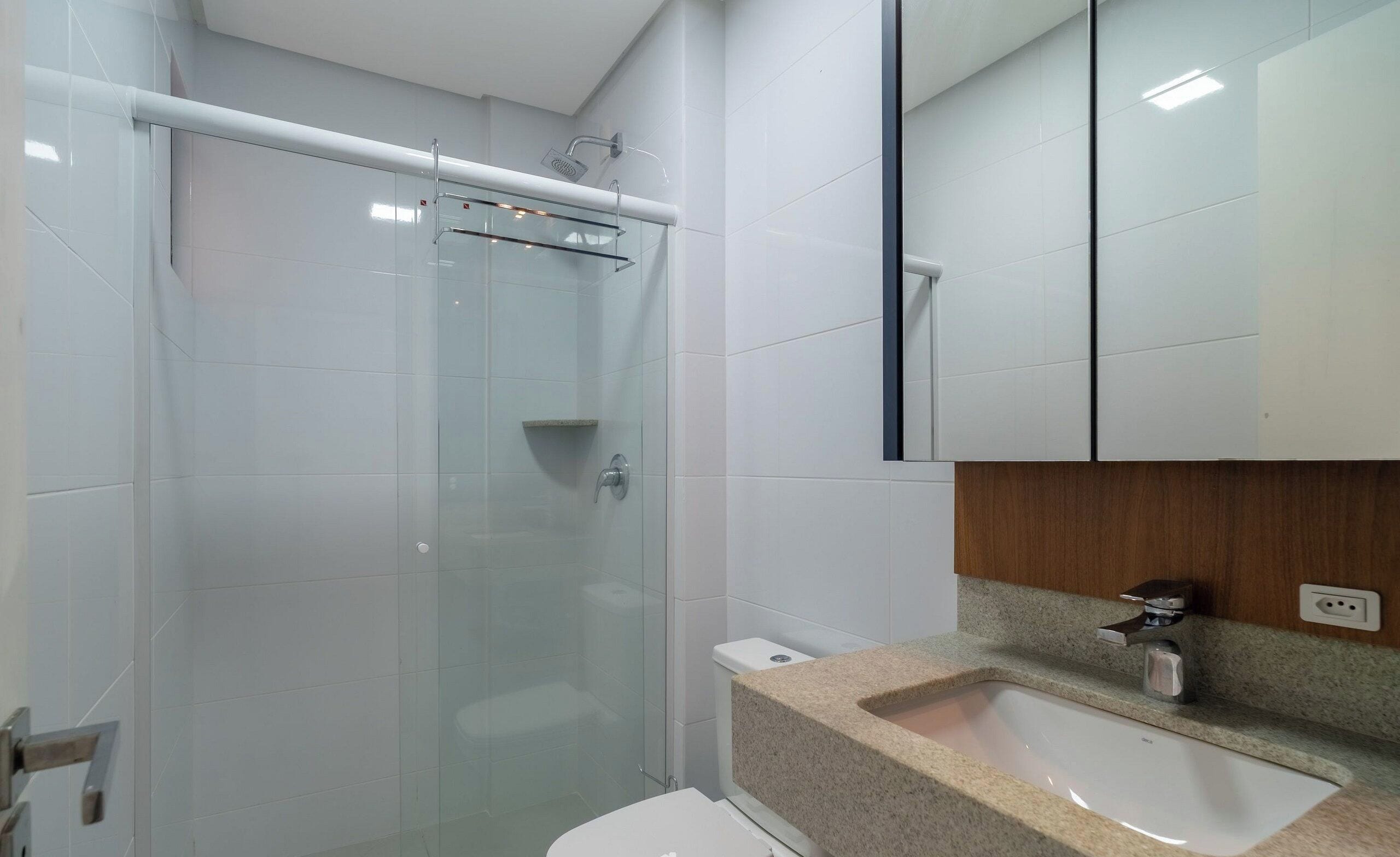 A modern bathroom with a glass-enclosed shower, a white toilet, and a granite countertop sink.