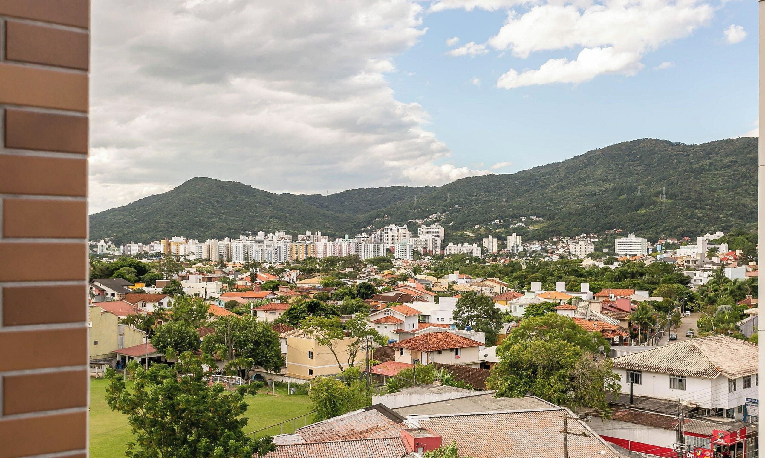 A residential area with a mix of single and multi-story buildings, surrounded by greenery and hills.