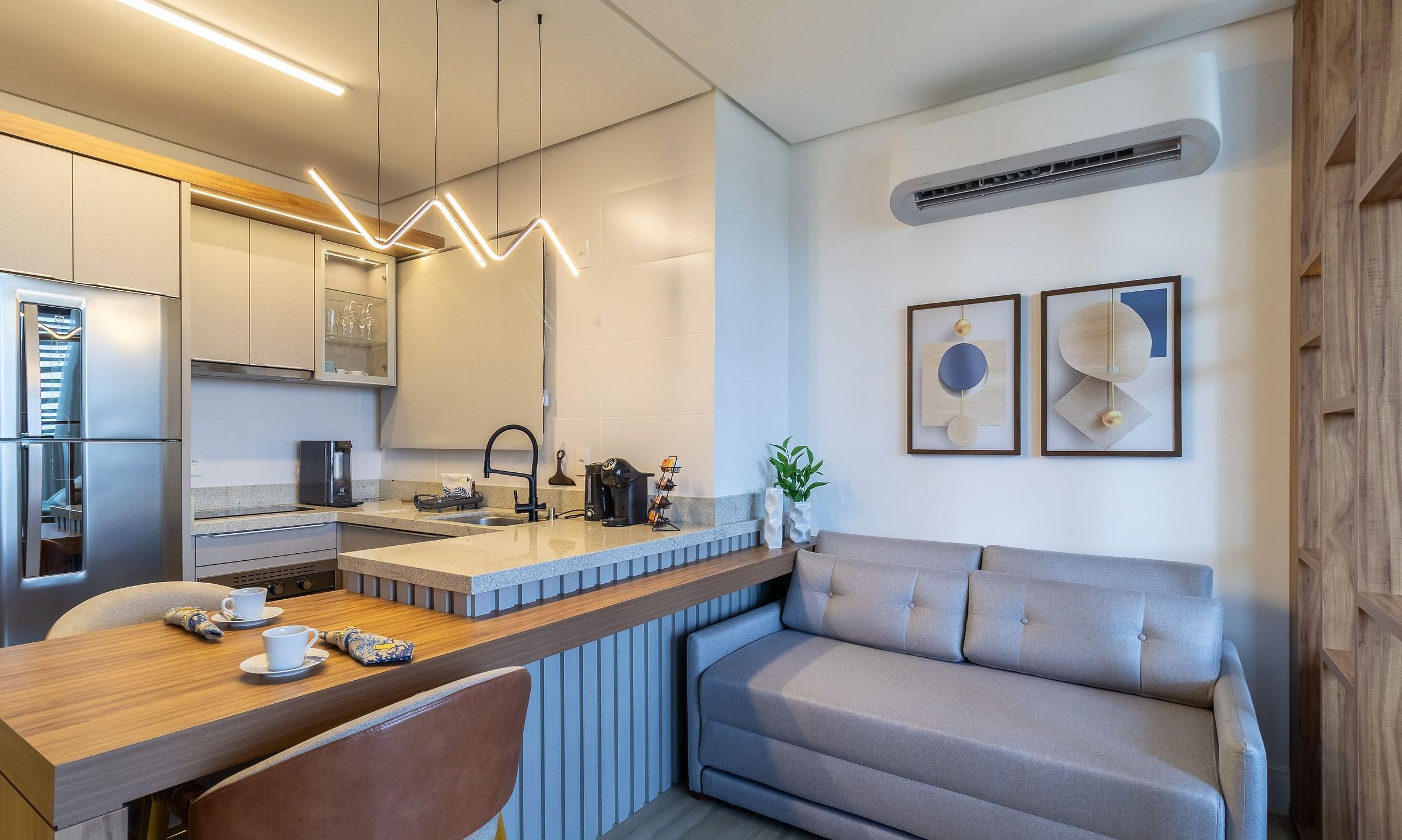 Eine moderne Küche mit Einbaukühlschrank, einer Kaffeemaschine und einem Essbereich mit Holztisch und grauem Sofa.