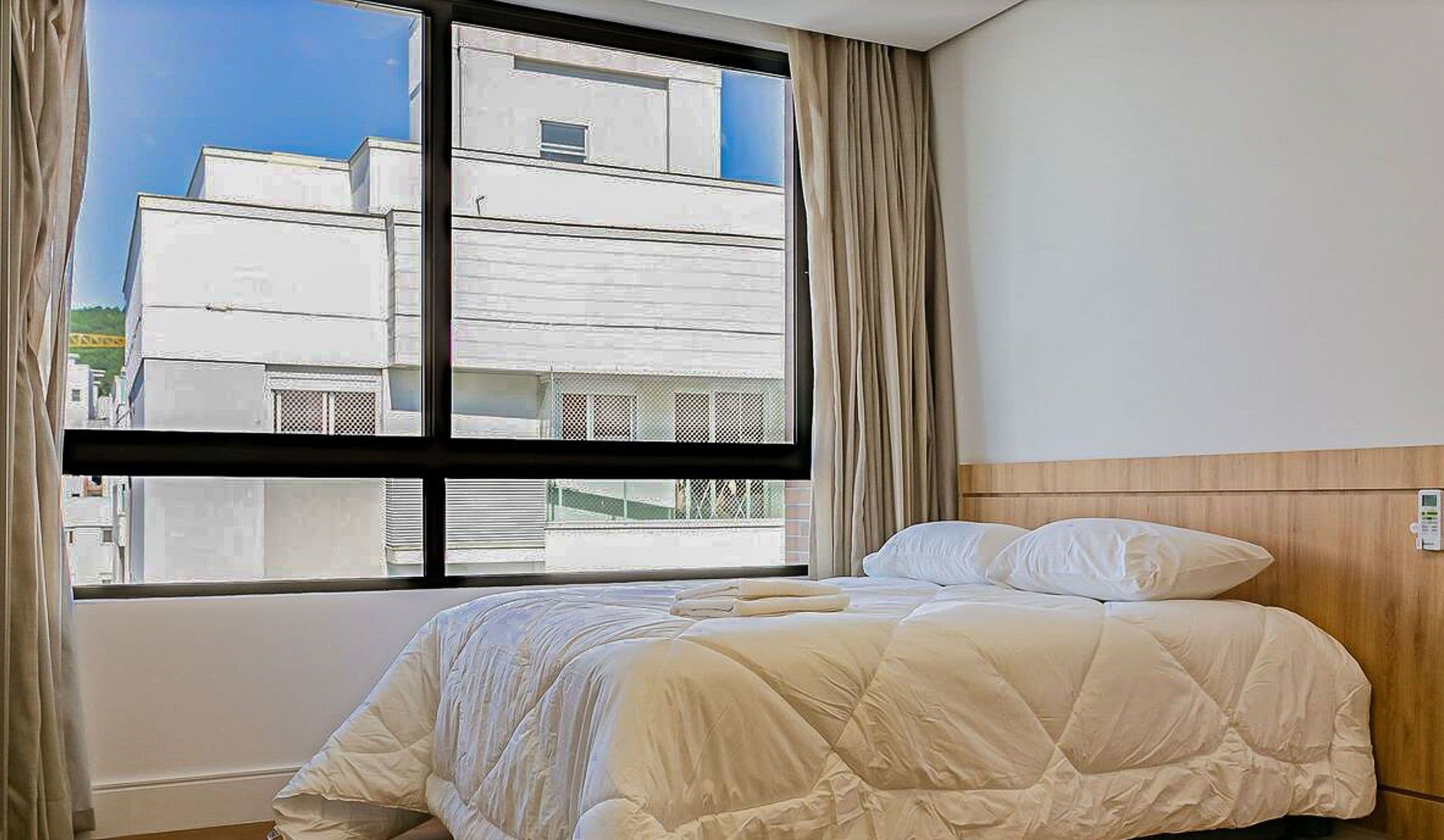 A hotel room with a bed, a window with curtains, and a view of buildings outside.