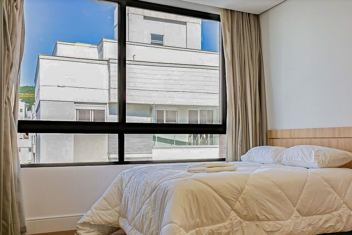 A hotel room with a bed, a window with curtains, and a view of a building outside.
