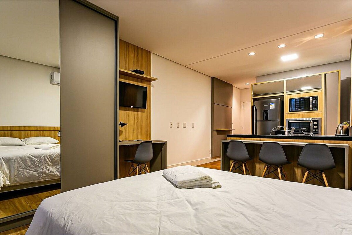 A hotel room with a bed, a desk with chairs, a kitchenette, and a bathroom.
