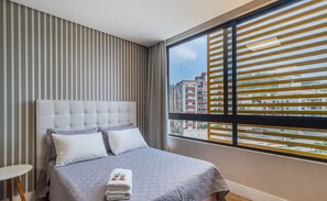 Une chambre d’hôtel avec un grand lit, des rideaux à rayures et une vue sur les immeubles par la fenêtre.