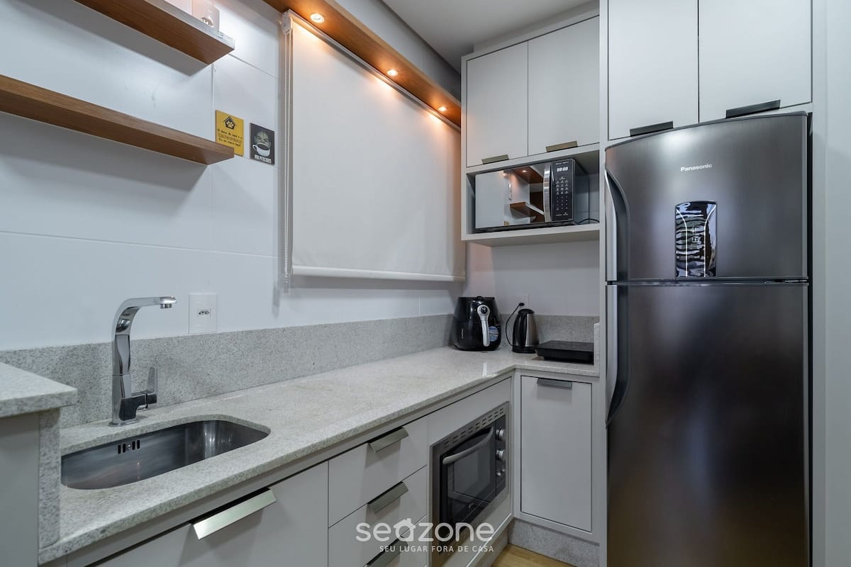 A modern kitchen with a stainless steel refrigerator, a built-in oven, a coffee maker, and a microwave.