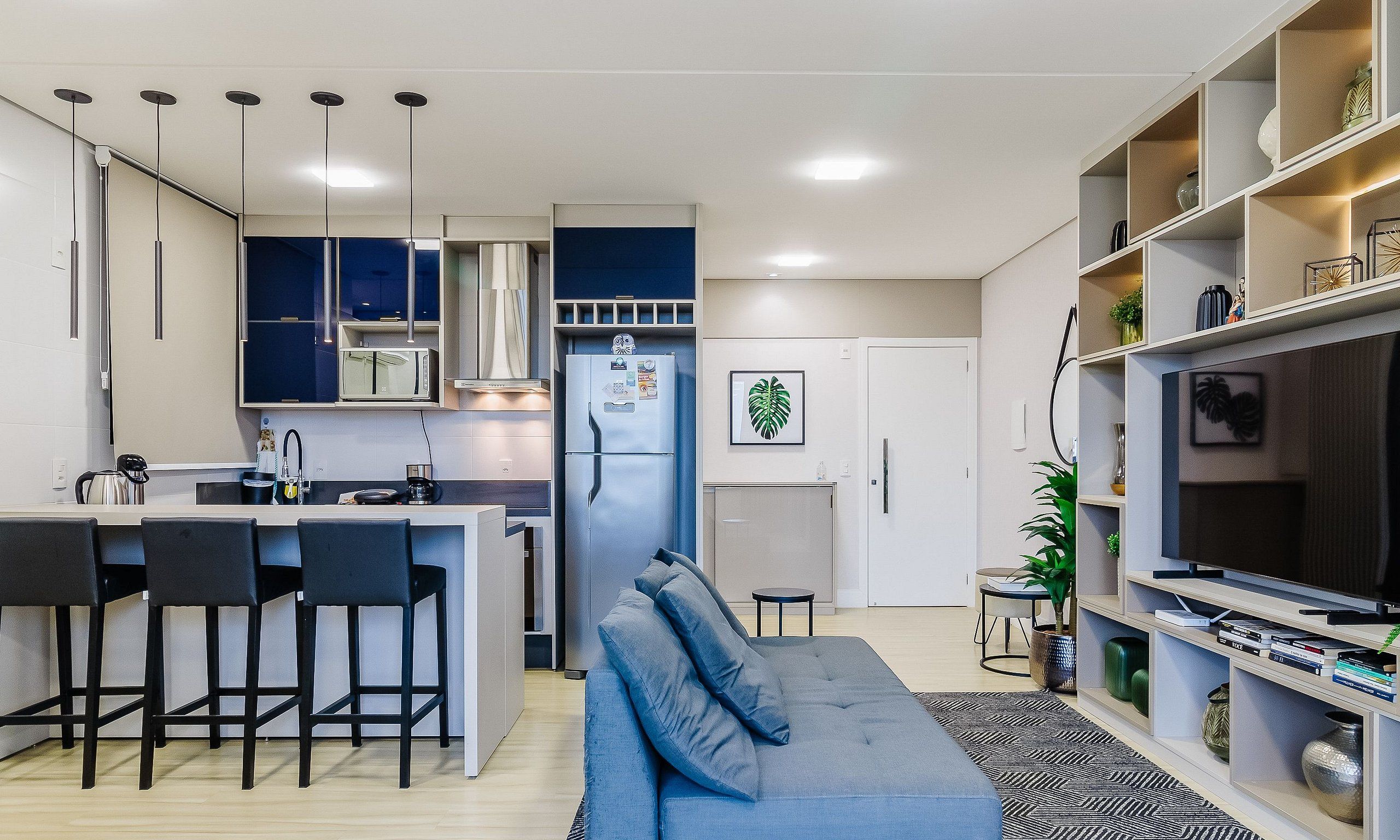 Een moderne keuken met een centraal eiland, barkrukken, een ingebouwde magnetron en een roestvrijstalen koelkast.