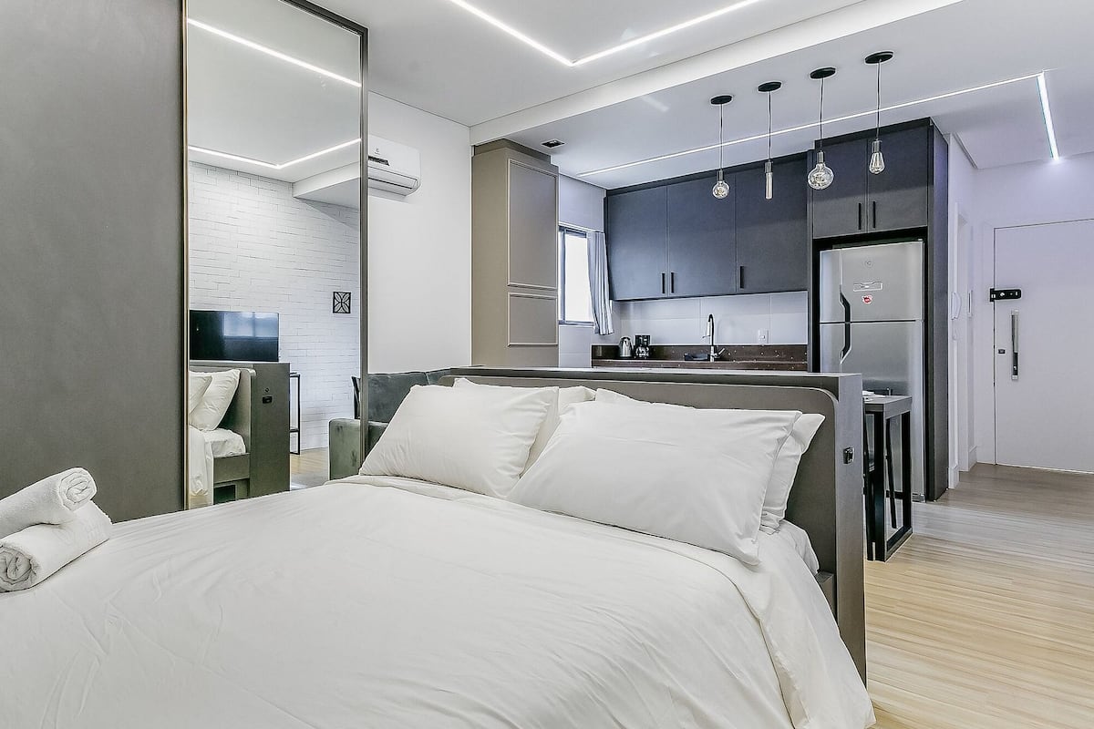 A modern hotel room with a large bed, a separate seating area, and a kitchenette.