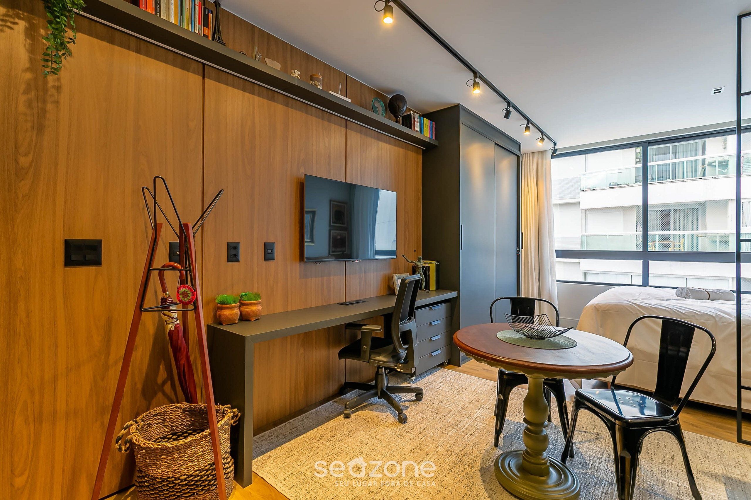 Habitación de hotel moderna con pared de madera, un escritorio con silla, una cama y un ventanal con vistas al edificio.