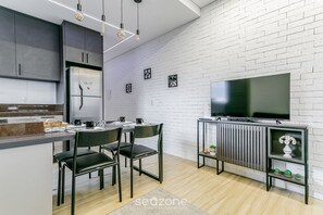 A modern kitchen with a built-in refrigerator, dining table with chairs, and a TV on a stand. - SSG Estúdios próximos a UFSC em Florianópolis (Florianópolis)