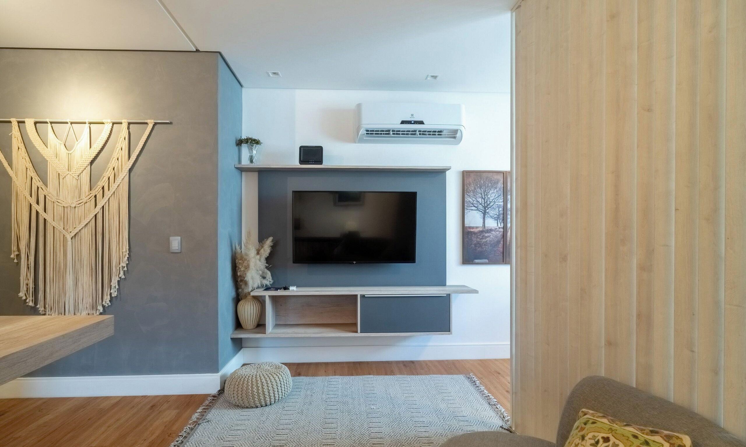 Un salon moderne avec un téléviseur à écran plat fixé au mur, un plancher en bois et une décoration murale en macramé.