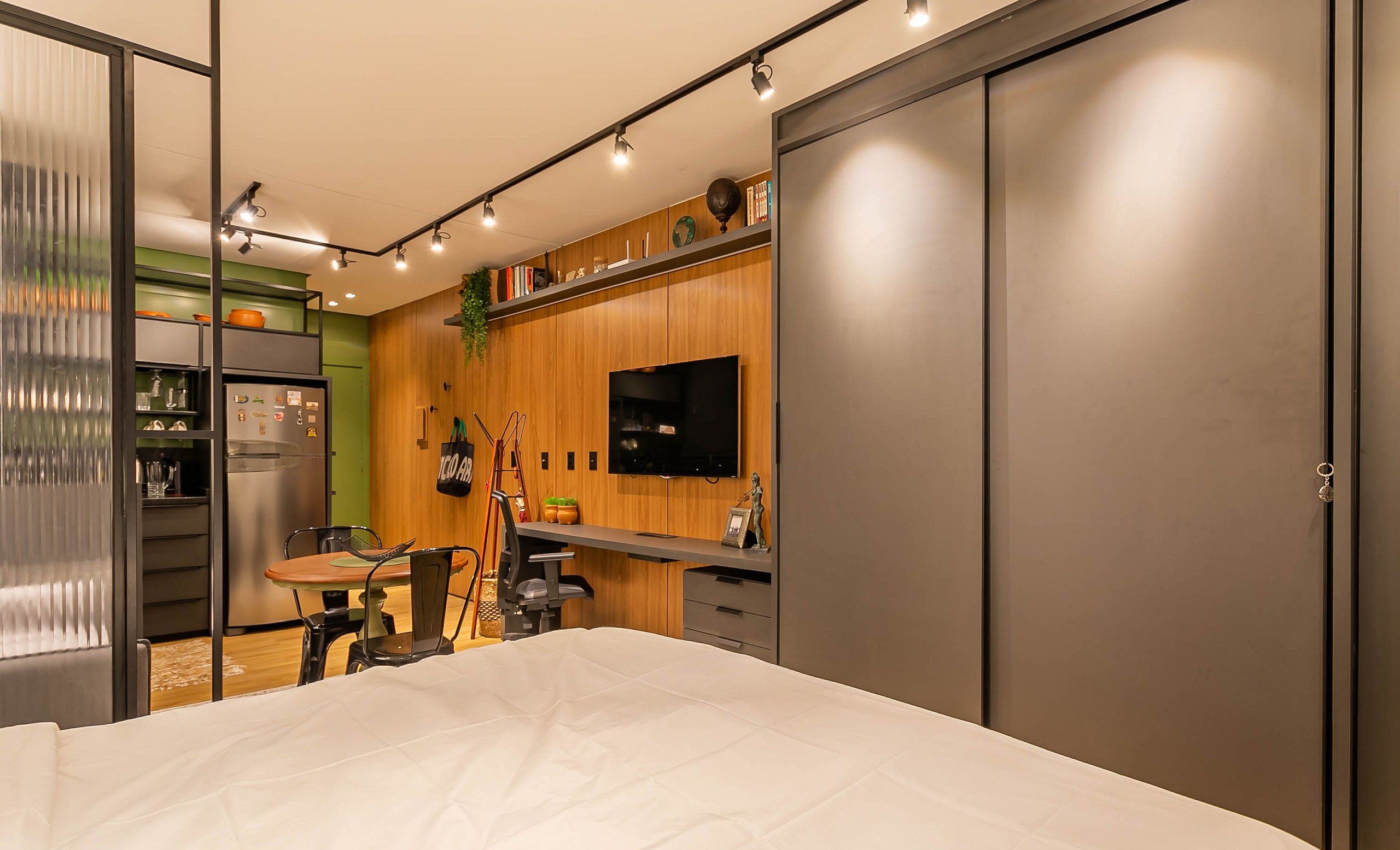 A modern bedroom with a bed, a TV mounted on the wall, a wooden cabinet, and a refrigerator.