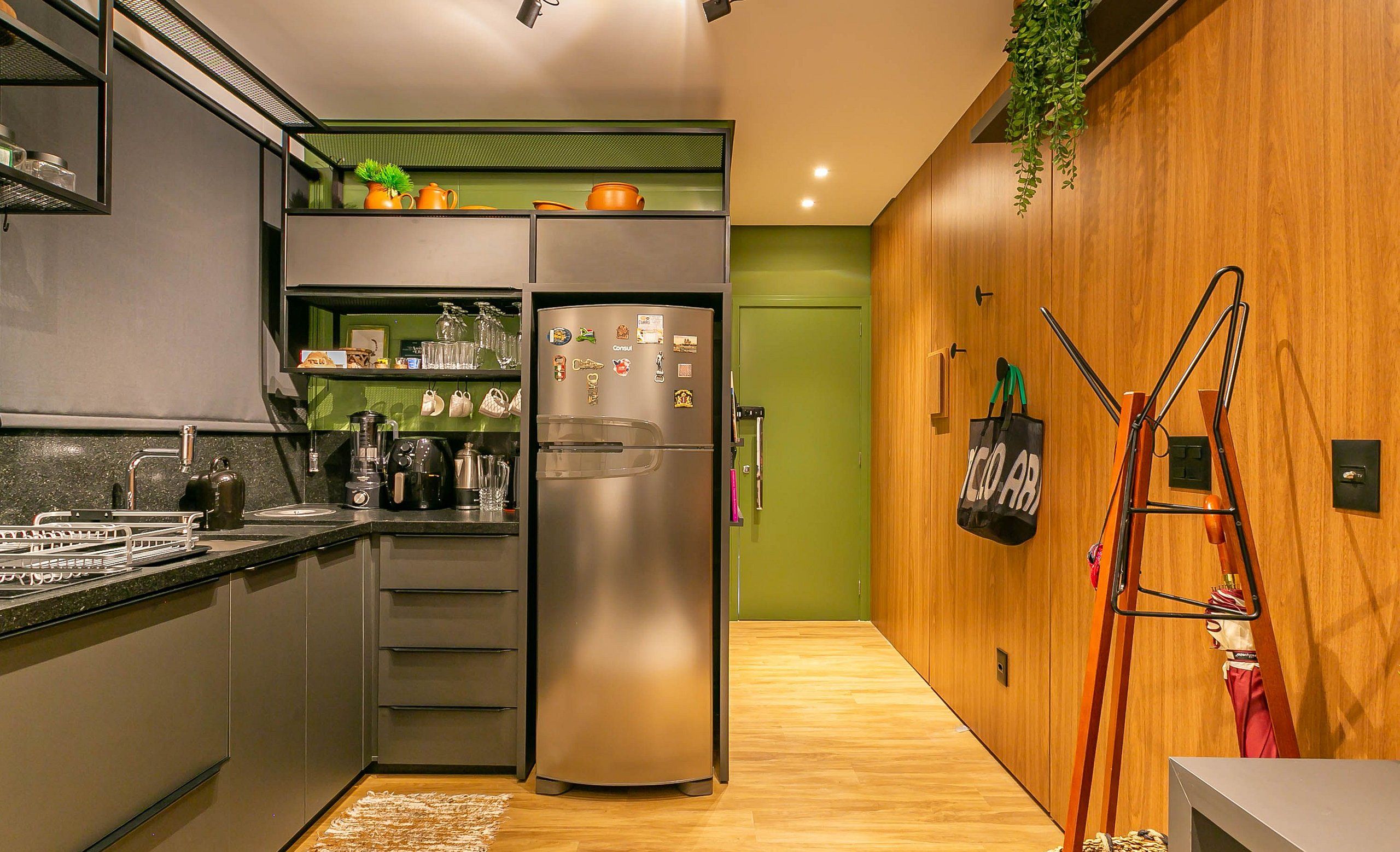 Eine moderne Küche mit einem eingebauten Kühlschrank, einer Kaffeemaschine und einem Spülbecken. Eine Holzvertäfelung mit einer hängenden Pflanze und einer Leiter ist zu sehen.