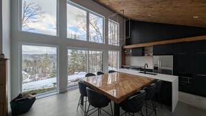 A modern kitchen with large windows, a wooden island, and black cabinets. - Havre du Mont * New Construction (st-come)