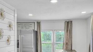 Une cuisine moderne dotée d’un réfrigérateur en acier inoxydable, d’un plancher en bois et d’une fenêtre avec des rideaux.