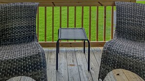 Une terrasse en bois avec deux fauteuils en osier et une petite table, donnant sur une pelouse verdoyante et un bâtiment situé au loin.