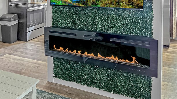 Un salon moderne avec un téléviseur à écran plat fixé au mur, le tout agrémenté d’un décor sur le thème de la nature. Sous le téléviseur, on aperçoit une cheminée avec un feu visible.
