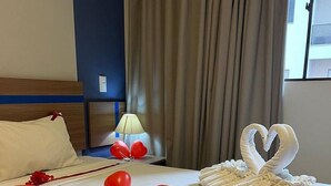 Een hotelkamer met een net opgemaakt bed, rode hartvormige ballonnen en een zwaan van handdoeken.