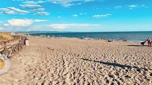 Una extensa playa de arena con un paseo marítimo de madera a la izquierda, que se adentra hacia el agua.