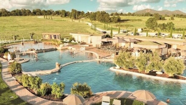 Un resort con varias piscinas, una piscina central grande y un área ajardinada con senderos y asientos.