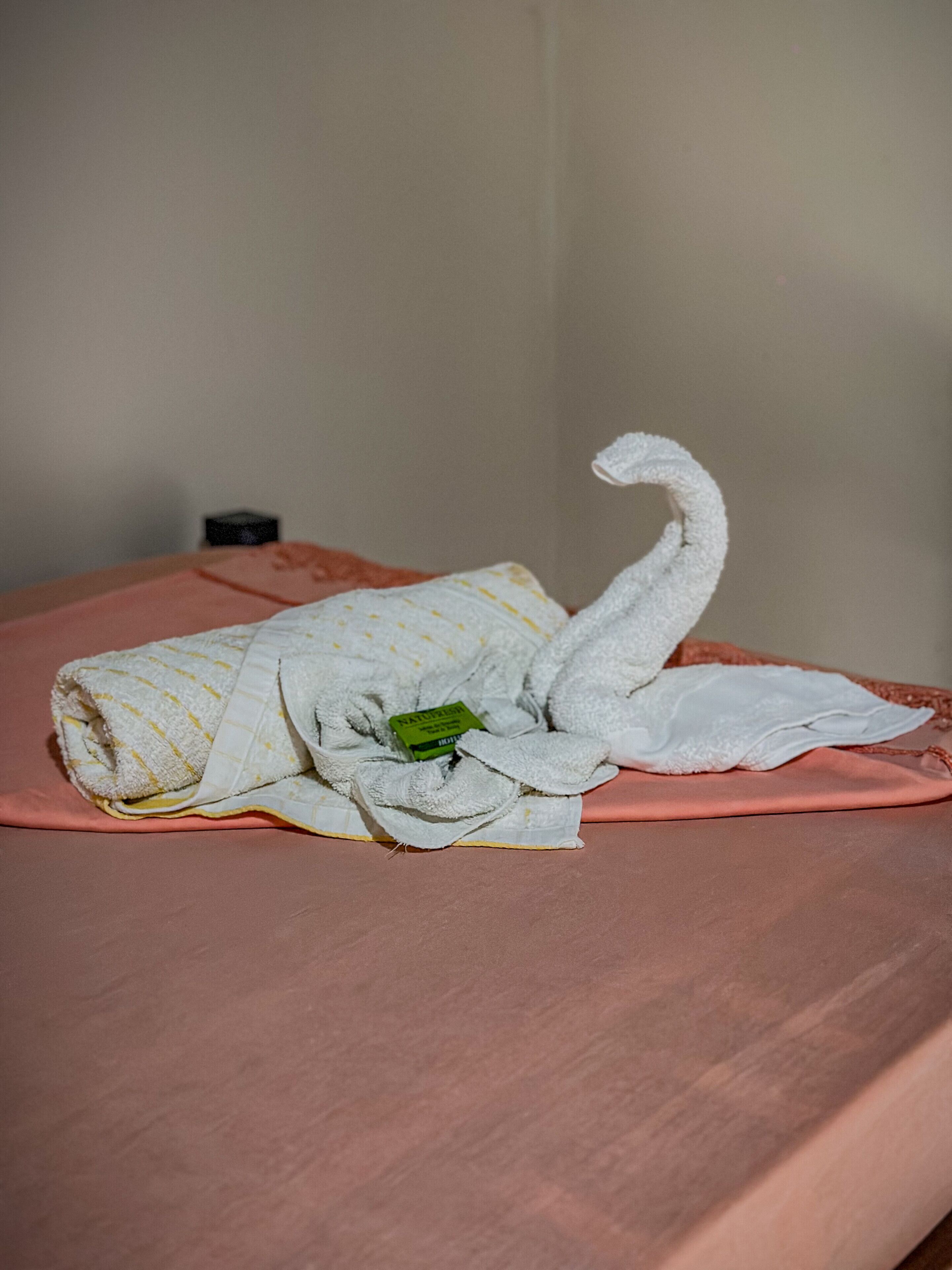 Un asciugamano piegato con cura con un'etichetta verde su un letto con una coperta rosa.