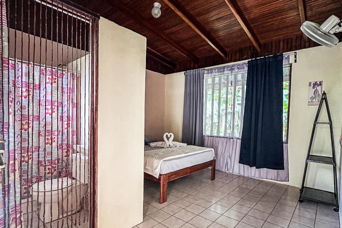 A room with a bed, a fan, and a window with curtains.