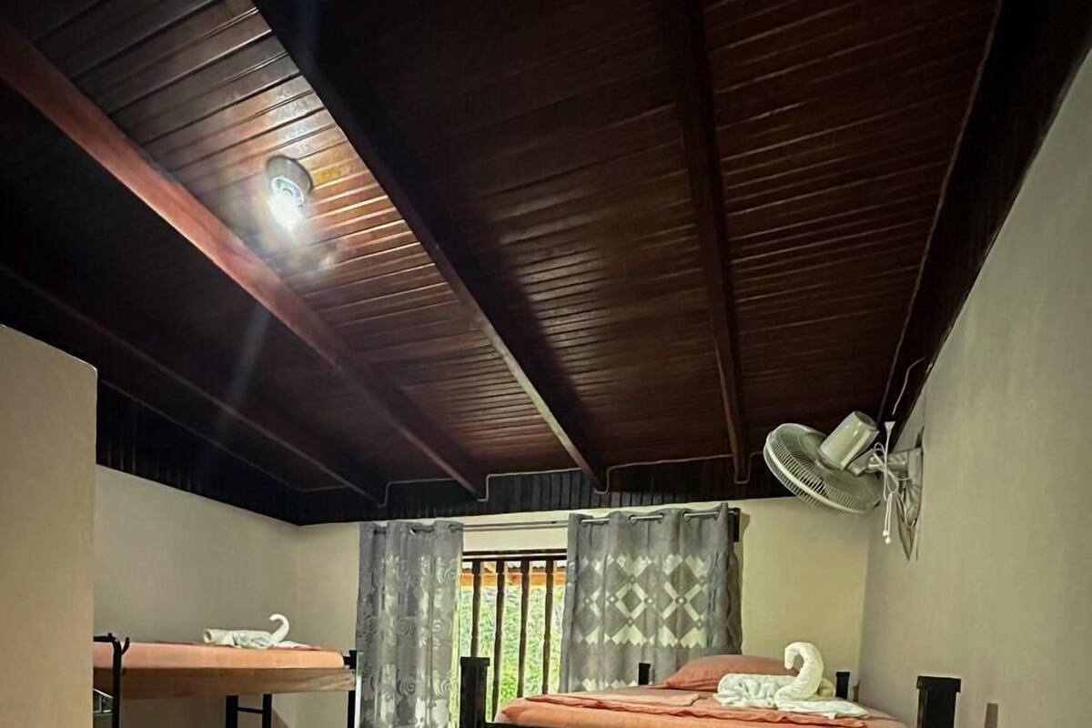 A dormitory room with bunk beds, a ceiling fan, and a window with curtains.