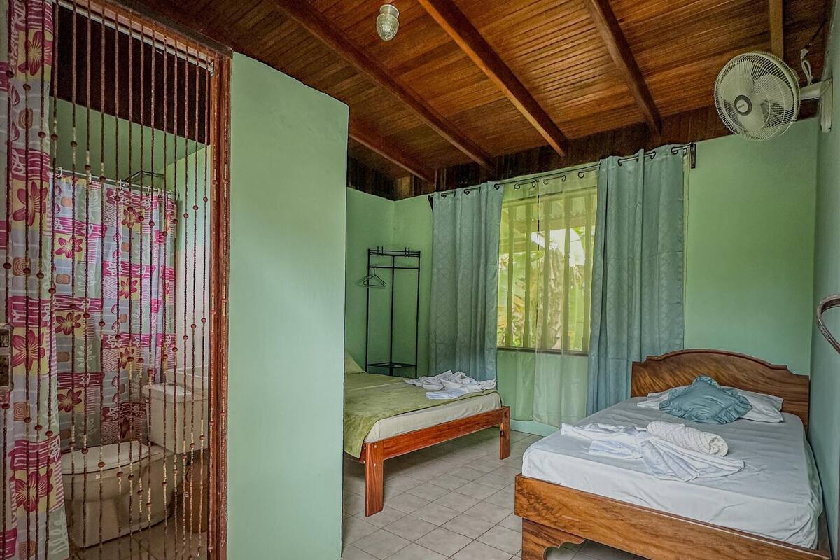 A room with two wooden beds, a tiled floor, a wooden ceiling, and a window with curtains.