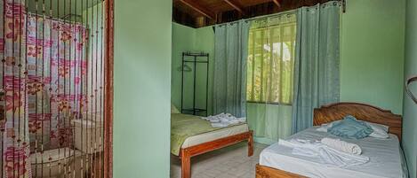 A room with two wooden beds, a tiled floor, a wooden ceiling, and a window with curtains.