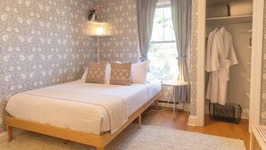 A bedroom with a wooden bed, patterned wallpaper, a bedside table with a lamp, and a walk-in closet with robes. - West End Bright Spot with Parking. (Portland)