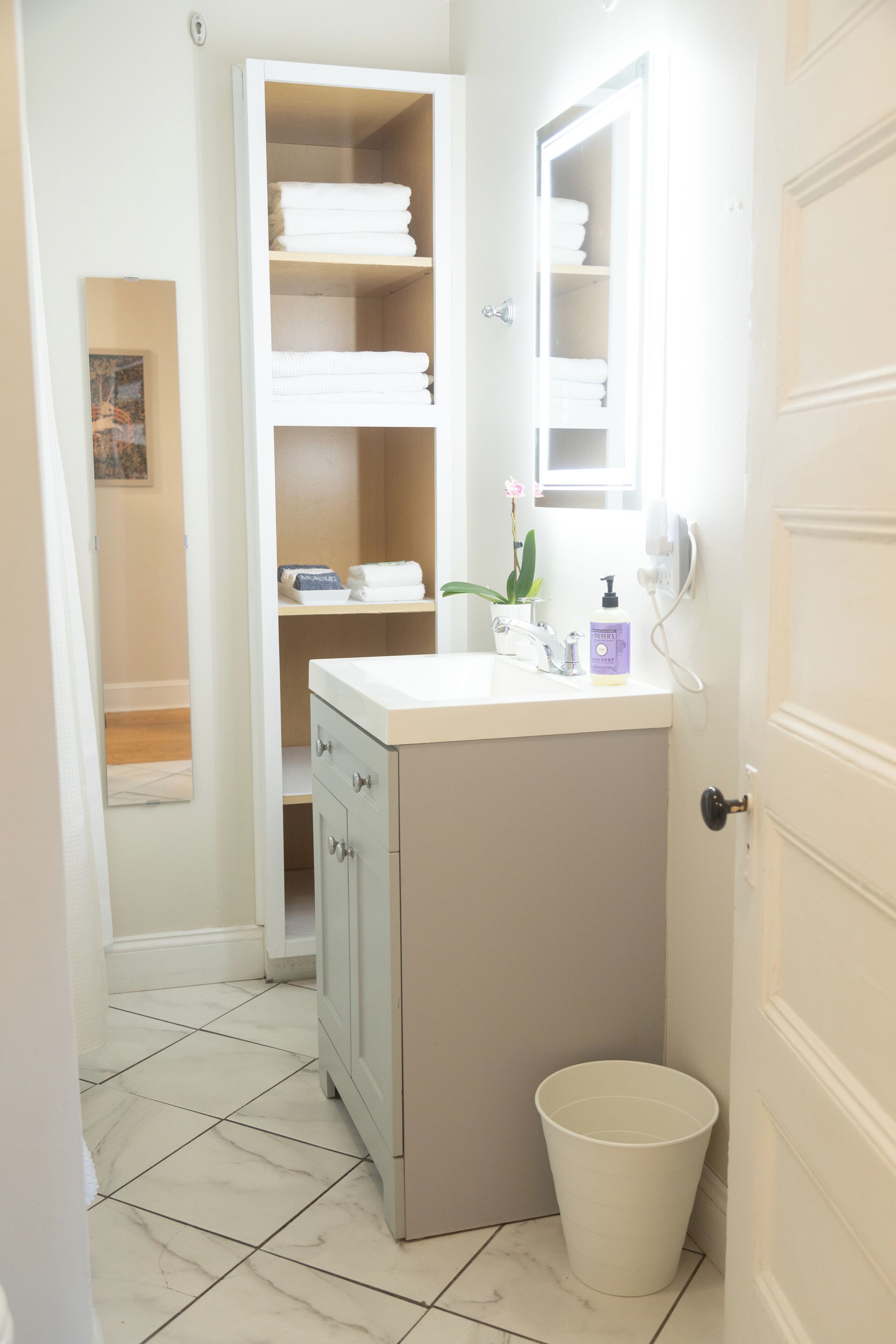 Une salle de bain avec un meuble-lavabo blanc, un miroir, un évier, des toilettes et un meuble de rangement.