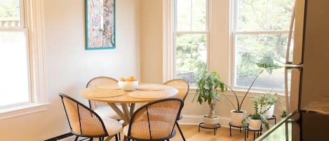 A dining area with a round table, four chairs, a bowl of fruit, and potted plants.