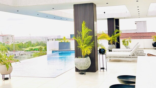 Un bar moderno en la azotea con vistas a una piscina, con un diseño minimalista que incluye taburetes de bar negros y plantas en macetas.