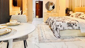 Una habitación de hotel moderna con suelo de mármol, una mesa de comedor redonda, una cama con ropa de cama estampada, un espejo y un equipo de aire acondicionado.